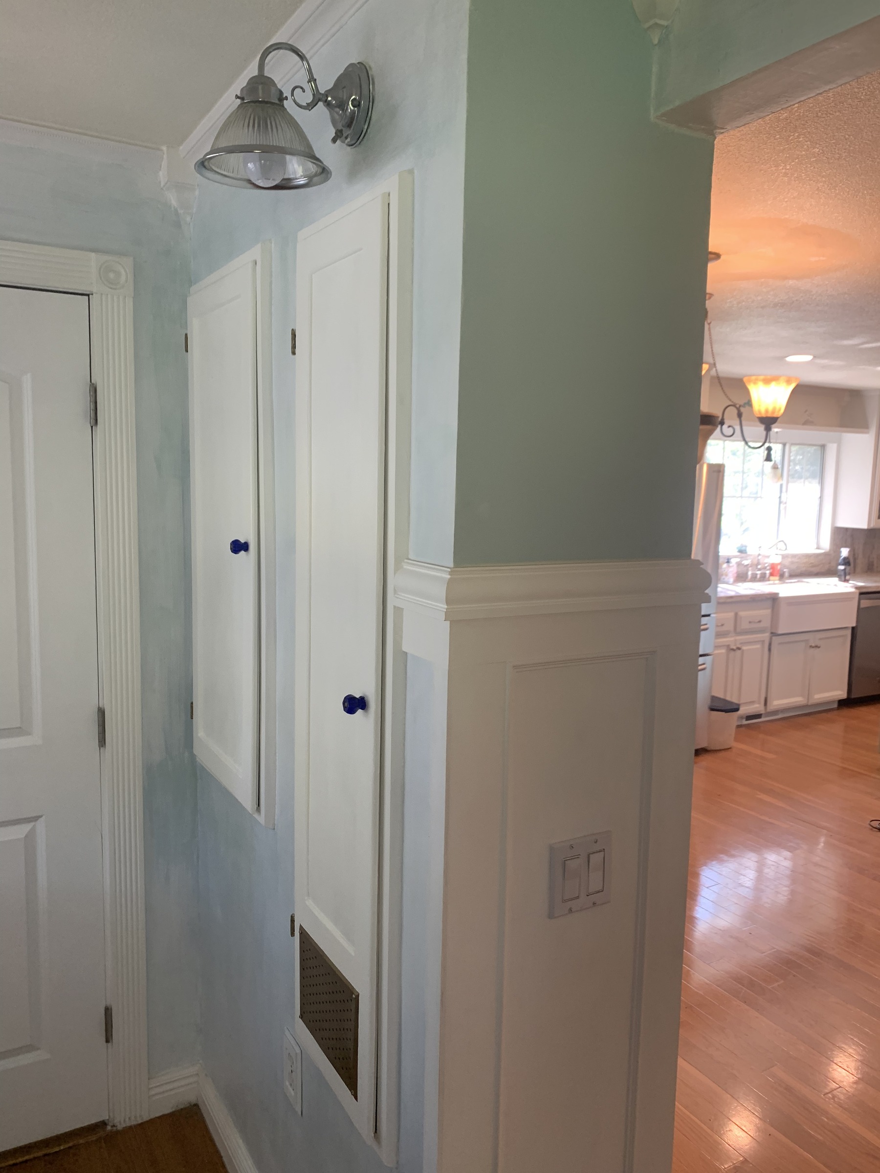 Finished ironing-board and breaker-box doors with small cobalt-blue glass knobs beside the paneled entry