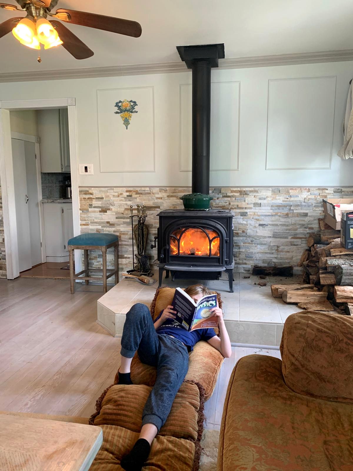 Child reading beside the lit Jøtul stove in the California farmhouse living room