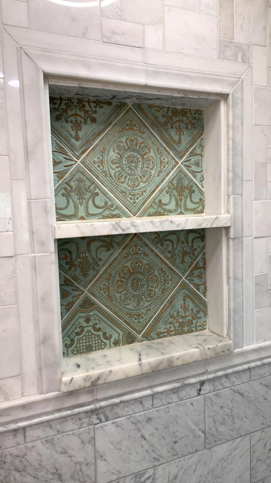 Aqua and warm bronze patterned tile inside a carefully framed marble shower niche
