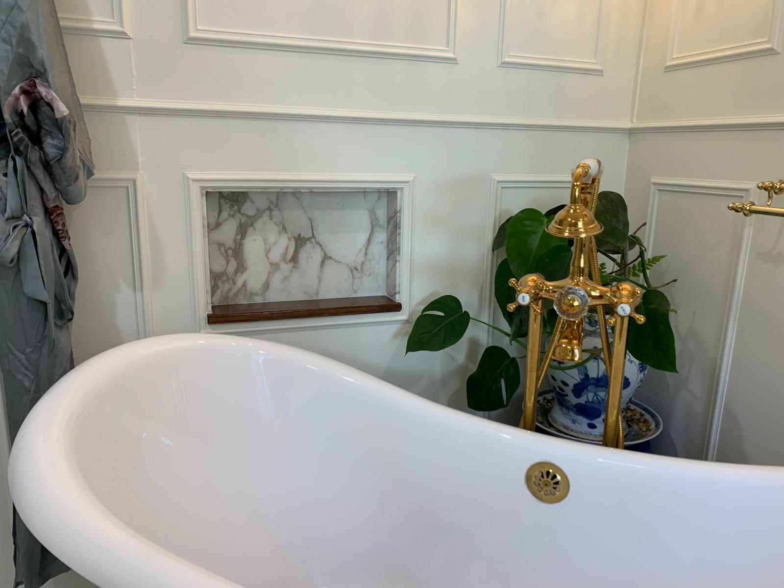Freestanding white bathtub beside a framed inset of salvaged I. Magnin marble and brass fixtures